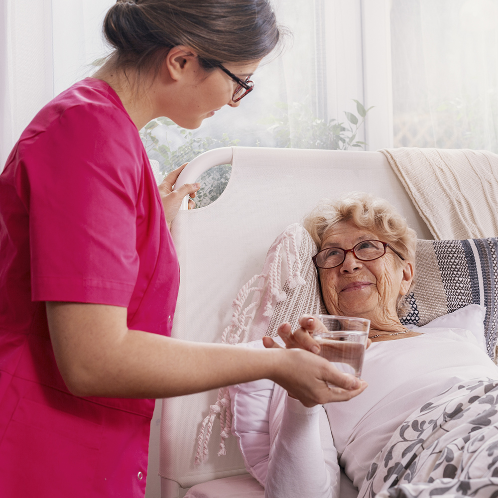 Beautiful young nurse serves tea to an elderly lady in a private Long Term Care Facilities In Ennis