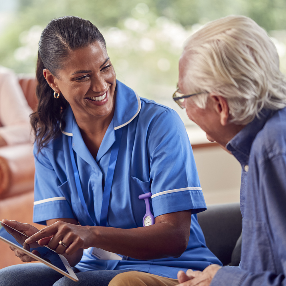 Senior Couple At Home With Man Talking To Female Nurse Or Care W Memory Care Ennis